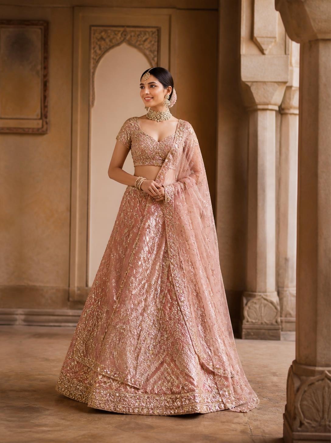 Bride in a rose-gold sequin embroidered lehenga with a matching net dupatta in a sandstone hall